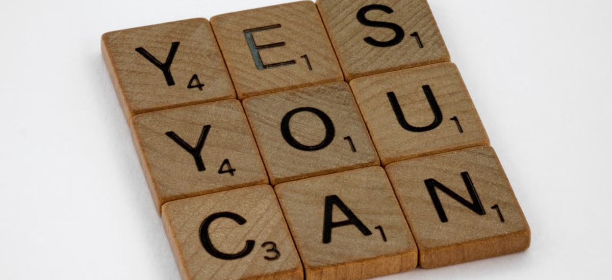 Wooden Scrabble tiles on white surface spelling 'Yes You Can,' promoting positivity and motivation.