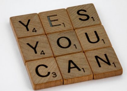 Wooden Scrabble tiles on white surface spelling 'Yes You Can,' promoting positivity and motivation.